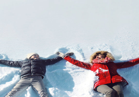 Happy mother and son playing and having fun together lying in the snow on a sunny winter day